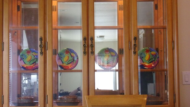 A wooden cabinet with glass doors, each containing a colorful glass plate. - $89/night for 2 people, plus $20/night for each additional person (Pahrump)