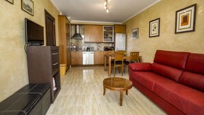 Um espaço de estar compacto com cozinha compacta, um sofá vermelho, uma mesa redonda pequena e uma TV em um móvel.