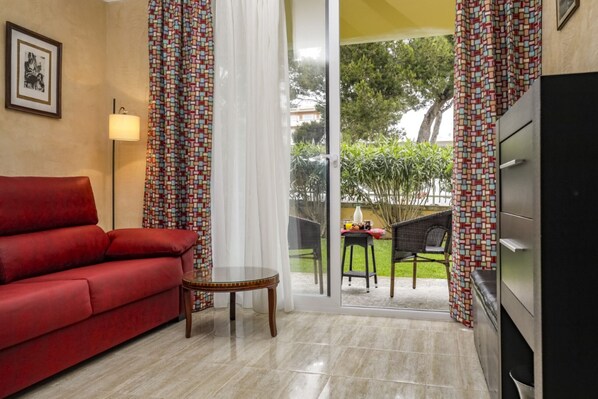 A living room with a red sofa, a small round table, and a TV stand. - Apartment close to the beach with terrace and communal pool, YourHouse Ronda Playa Holidays (Can Picafort)