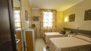 Quarto de hotel com duas camas, uma mesa, um espelho e uma janela com cortinas florais.
