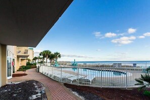 A pool area with a view of the ocean, a fenced deck, and a building with a balcony.