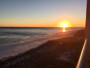 Ein Sonnenuntergang über einem Strand mit einer Promenade und einigen Spaziergängern.