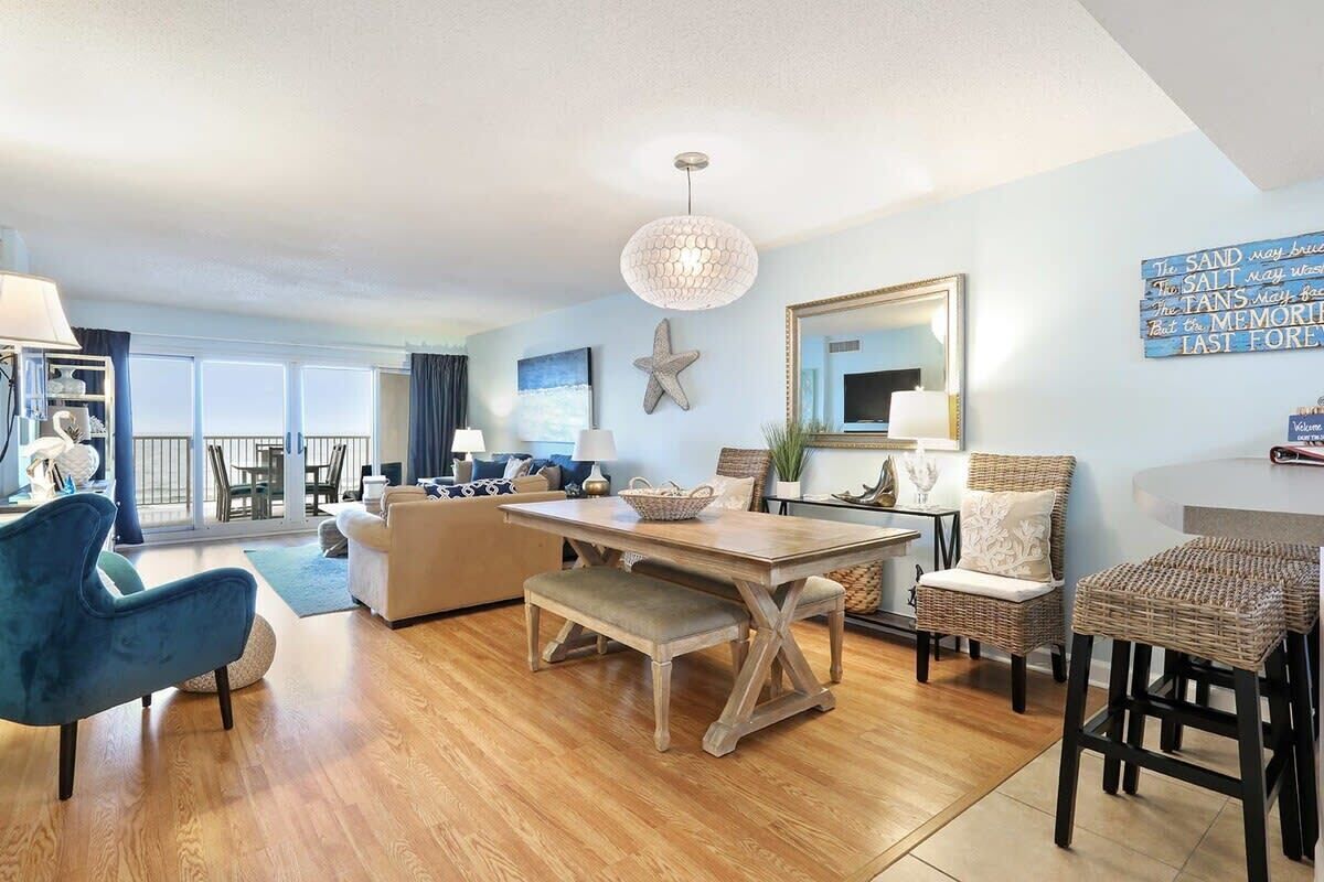 A spacious living area with a wooden dining table, blue armchairs, a bench, and a large starfish decoration.