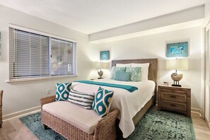 A bedroom with a bed, a nightstand, a wicker sofa, a window with blinds, and two wall-mounted lamps.