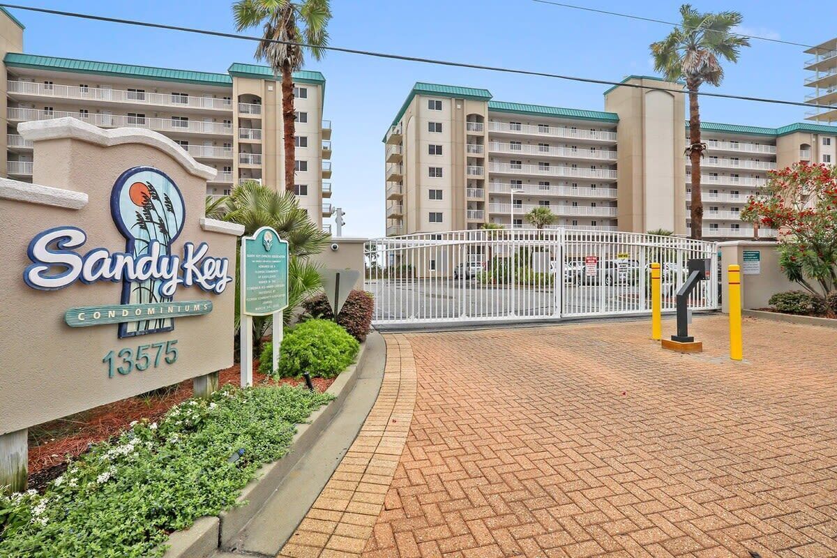 A gated entrance to a building complex with a sign reading 'Sandy Key Condominiums 13575'.