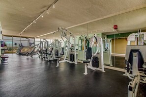 A gym with various exercise machines, a mirrored wall, and a large window.