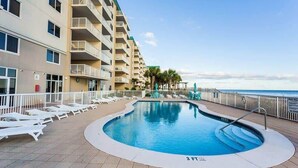 A swimming pool with lounge chairs, a building with balconies, and a view of the ocean. - Sandy Key 635: 2 BD/2BH, 6th floor (Pensacola)