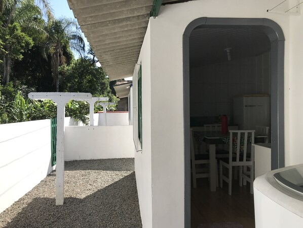 A small, enclosed patio area with a white wall, a concrete roof, and a white door leading inside.