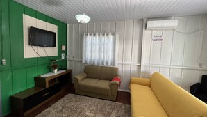 Ein Wohnzimmer mit grüner Wand, einem beigen Sofa, einem gelben Sofa, einem an der Wand montierten Flachbildfernseher und einem Deckenventilator.