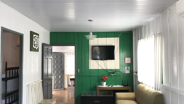 Ein Wohnzimmer mit einer grünen Akzentwand, einem flachbildfernseher, der über einem Holzkonsole angebracht ist, und einem beigen Sofa.