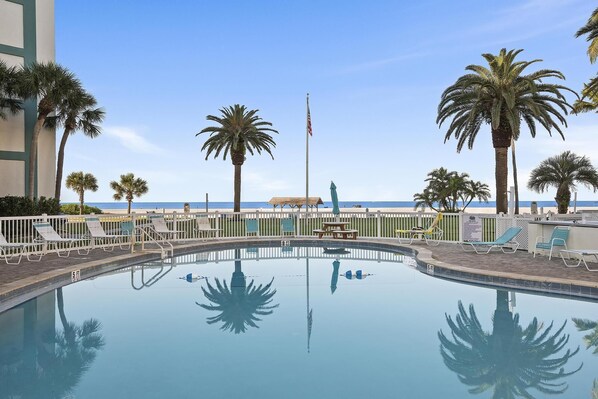 A clear pool with lounge chairs and palm trees, a flag, and a view of the beach. - Siesta Key Beach Resort Jamaica Royale (Siesta Key)