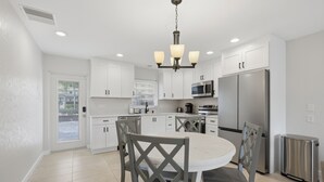 A modern kitchen with white cabinets, a stainless steel refrigerator, and a dining area with gray chairs. - Siesta Key Beach Resort Jamaica Royale (Siesta Key)