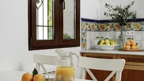 Una cucina con un tavolo bianco apparecchiato per la colazione, con arance, una brocca di succo d'arancia e bicchieri.
