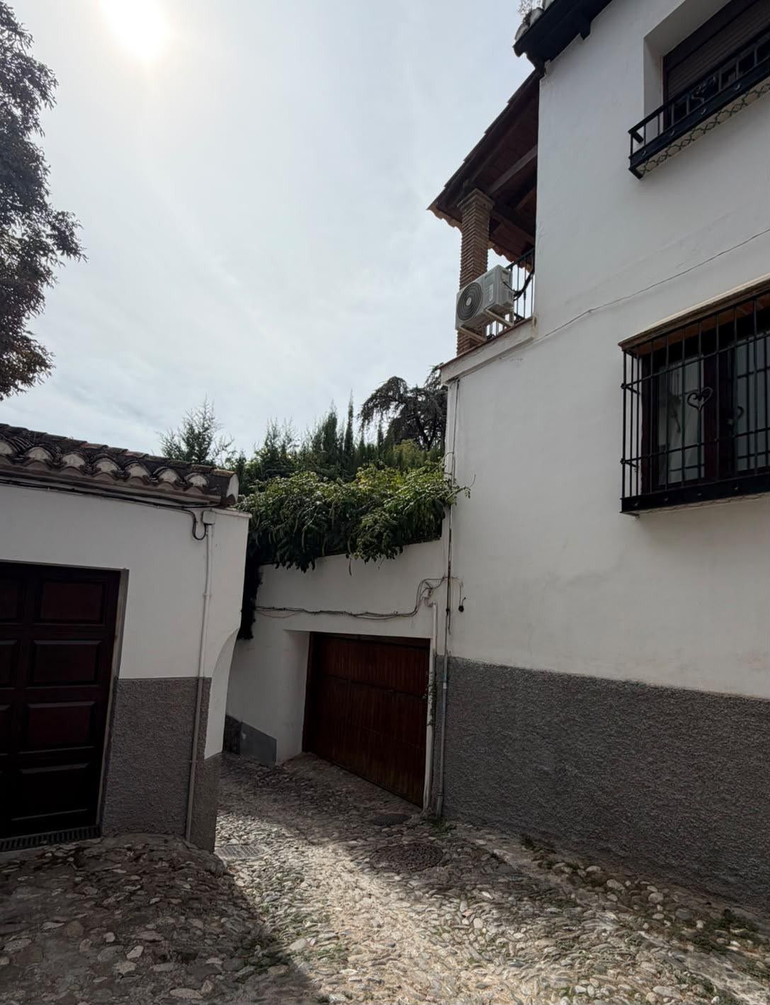 Un patio con un edificio blanco, una puerta de madera y una ventana con reja de metal.