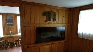 En stuga med träpanel på insidan, en öppen spis, ett matbord och en säng.