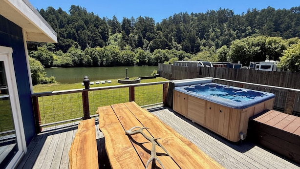 Eine Holzterrasse mit Whirlpool, Tisch und Stühlen mit Blick auf einen See und einen Wald.