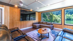 Ein modernes Wohnzimmer mit Ecksofa, Couchtisch und großen Fenstern, die einen Ausblick ins Freie bieten.
