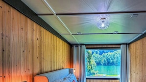 Ein Schlafzimmer mit einem Bett, einem Nachttisch, einer Lampe und einem Fenster mit Blick auf Bäume.