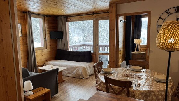 A cozy cabin with a bed, a dining table set for two, and a TV mounted on the wall. - Le Portail 19 - Beautiful 2-room apartment, overlooking the slopes and the valley (LES AVANCHERS VALMOREL)