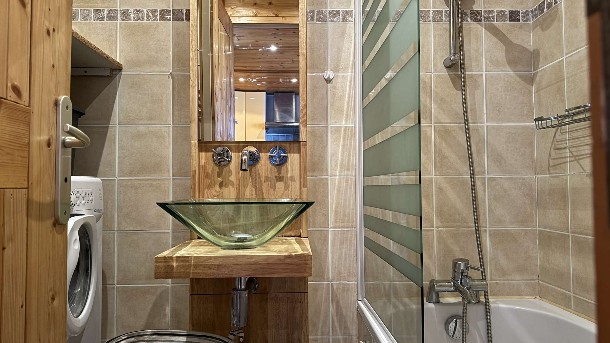 Un baño con lavamanos de vidrio, muebles de madera, lavadora, bañera y ducha.