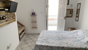 Une chambre avec un lit, un téléviseur fixé sur une étagère en bois, un panneau indiquant la présence d’une connexion Wi-Fi, une petite table et une fenêtre donnant sur un paysage agréable.