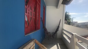 Un balcon avec un banc en bois, des portes rouges et un hamac.