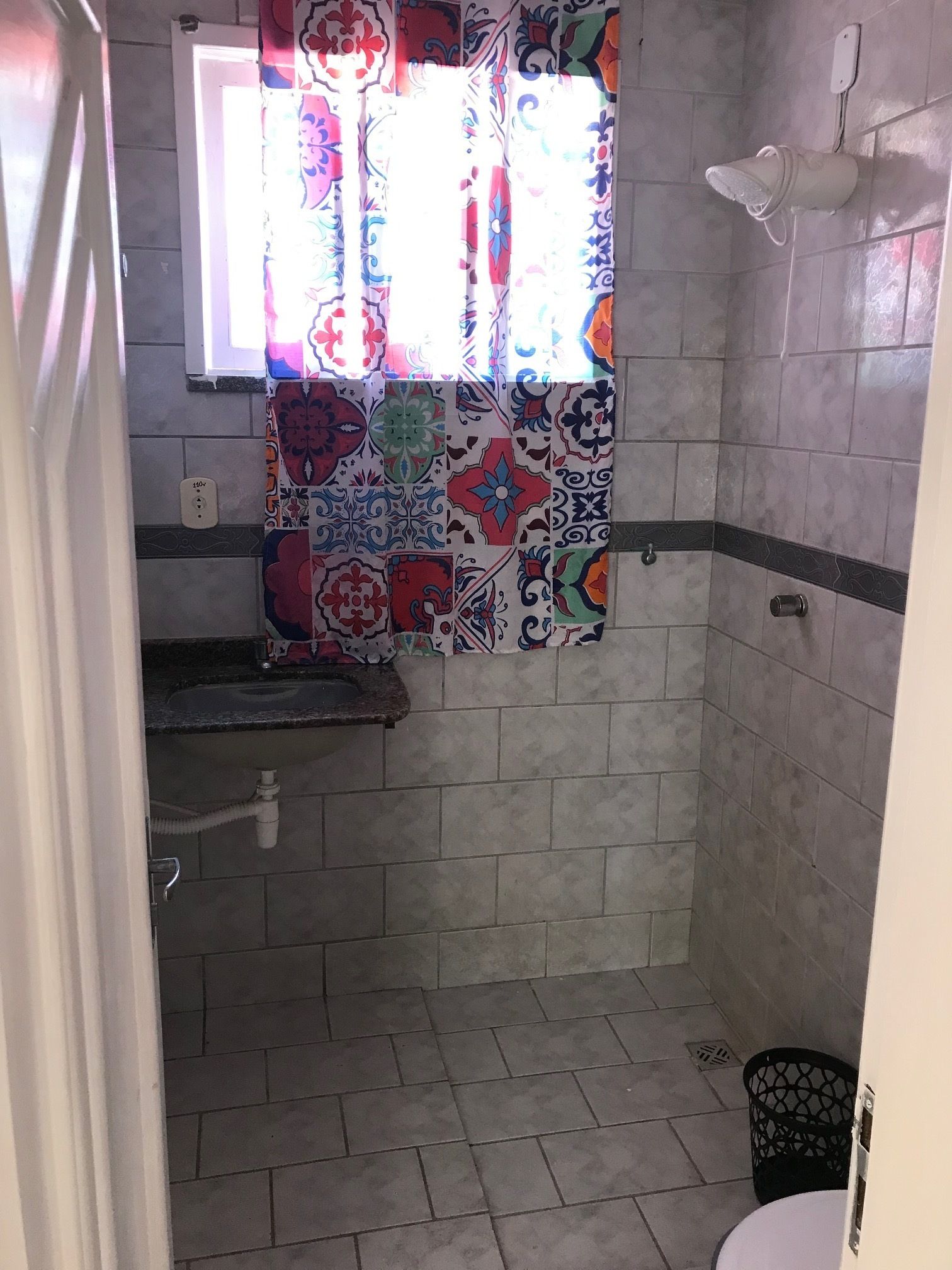 A bathroom with patterned tiles, a shower curtain, a window, and a towel rack.