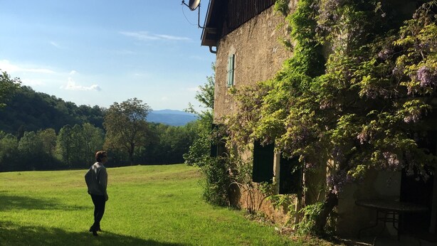 Une personne se tient dans un champ herbeux, à proximité d’un bâtiment doté d’une antenne parabolique et d’une table.
