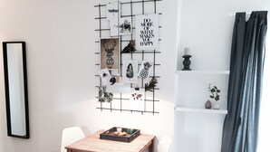 A modern room with a wooden table, white chairs, a grid wall with various framed pictures, and a dark curtain.