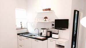 A modern kitchen with white cabinets, a black countertop, and a flat-screen TV mounted above the sink.