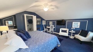 Una camera da letto con un letto grande, una scrivania, una sedia, una TV e una ventola a soffitto.