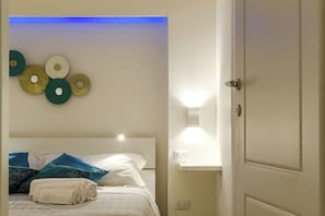 A hotel room with a bed, wall-mounted decorative items, a bedside table with a lamp, and a door.