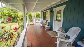 A covered porch with a wooden floor, white wicker chairs, and a small table with a vase. - Sleeping Giant Cottage with Plunge Pool TNVC #1244 (Kapaa)
