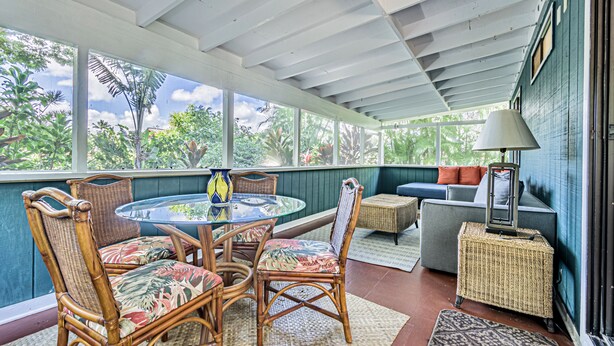 A covered patio area with wicker furniture, a round table, and a view of greenery. - Sleeping Giant Cottage with Plunge Pool TNVC #1244 (Kapaa)