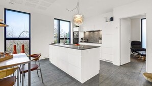 Une cuisine moderne dotée d’un îlot central, de grandes fenêtres et d’un coin repas avec des chaises.