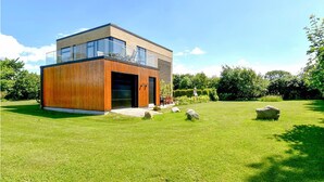 Une maison moderne avec une façade en bois, une véranda en verre et une pelouse bien entretenue.