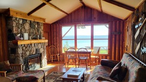 Interior acogedor de una cabaña con chimenea de piedra, muebles de madera y un amplio ventanal con vistas al lago.
