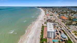 An aerial view of a coastal town with a wide sandy beach, a marina, and a mix of residential and commercial buildings.