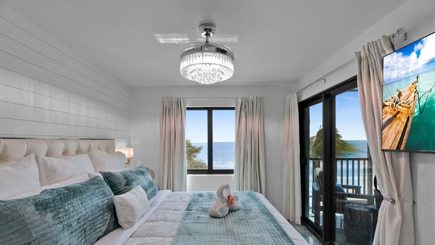 A bedroom with a large bed, a chandelier, a TV, and a view of the ocean.