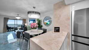 A modern hotel lobby with a marble reception desk, a chandelier, a dining area with a view, and a large window.