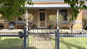 Une maison à deux étages, construite en briques, avec un porche à l’avant, le numéro « 228 » sur la porte et un petit jardin agrémenté de plantes en pot.