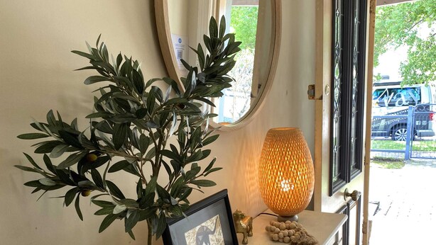 Une plante en pot, un tableau encadré et une lampe décorative sur une table en bois près d’une fenêtre.