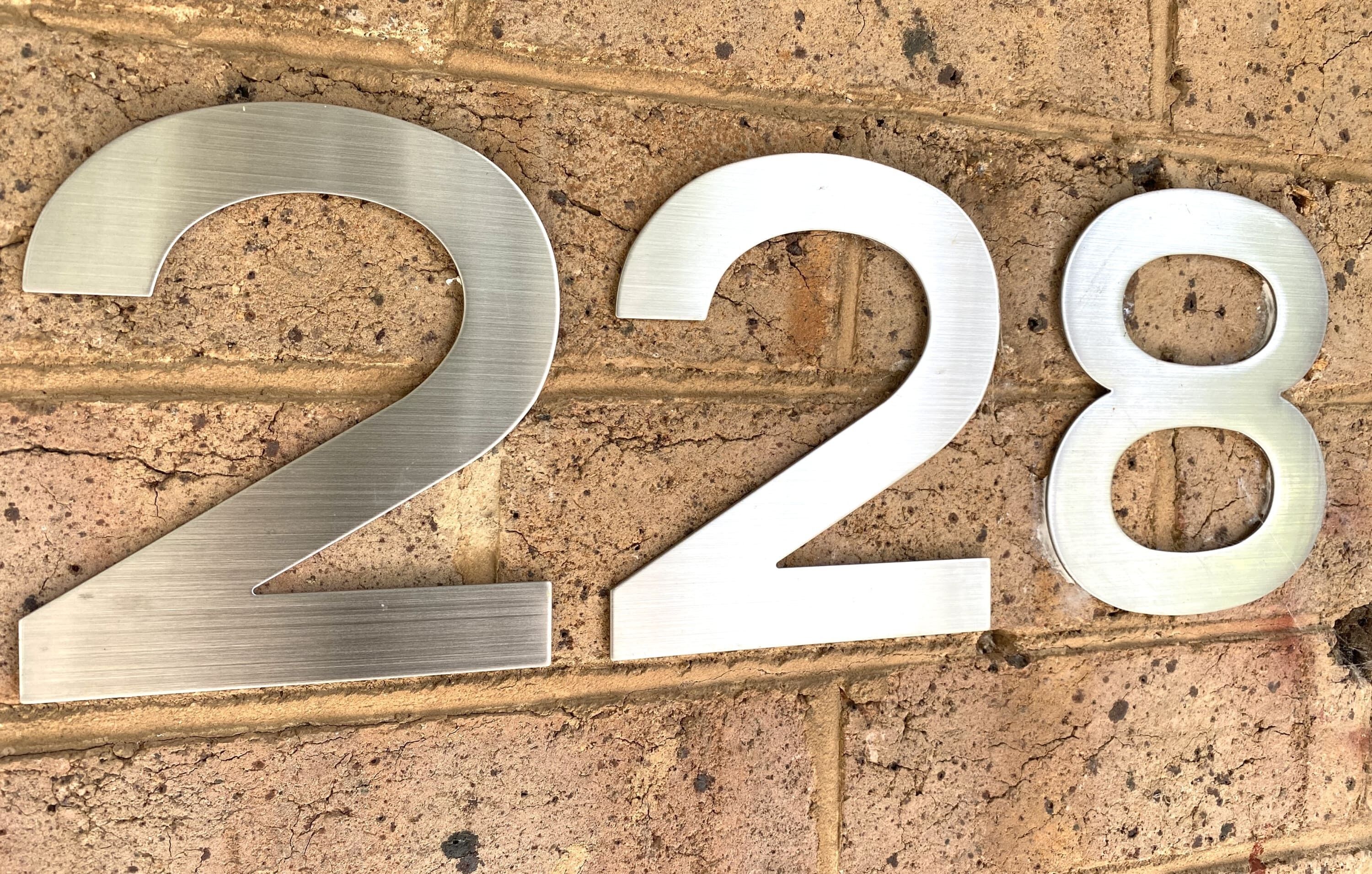 Un número '228' de metal adherido a una pared de ladrillo texturizada.