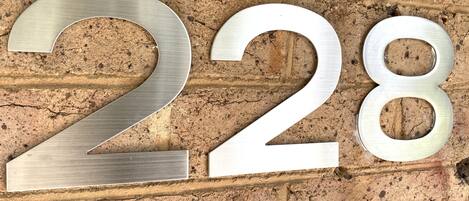 Un número '228' de metal adherido a una pared de ladrillo texturizada.