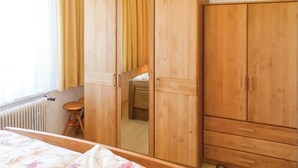 Une chambre avec des armoires en bois, un radiateur, un lit avec une literie à motifs floraux et une fenêtre avec des rideaux.