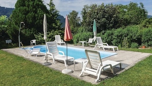 Une piscine entourée de verdure et d’arbres, avec des chaises longues et des parasols.