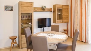 Un coin repas comprenant une table ronde, quatre chaises, un téléviseur et des meubles en bois dotés de portes en verre.