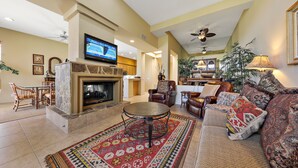 A living room with a fireplace, a television, a dining area, and a seating area with a patterned rug. - 122LQ LOOKING NORTH/WEST ON THE NICKLAUS PRIVATE WHAT AN AWSOME MOUNTAIN VIEW AND QUIET (La Quinta)