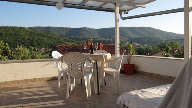A terrace with a table and chairs, a potted plant, and a bottle of champagne.