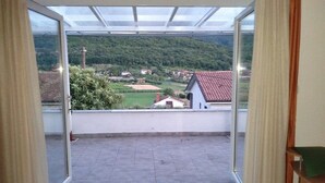A room with a large glass door leading to a balcony with a view of a rural landscape.